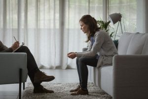 an adult woman sits with a therapist figuring out how treating trauma as the root of addiction could help her