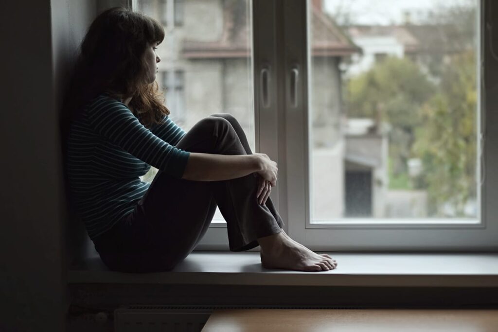woman sitting near window thinking about the effects of binge drinking on her mental health