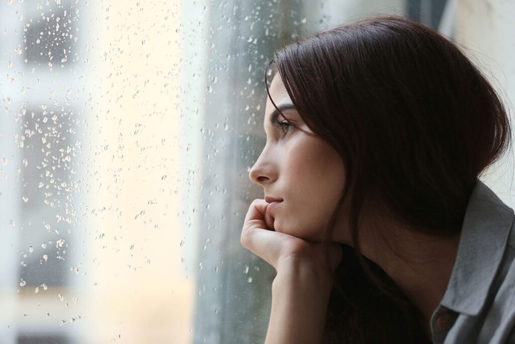 woman peering out the window thinking about the signs of alcohol withdrawal