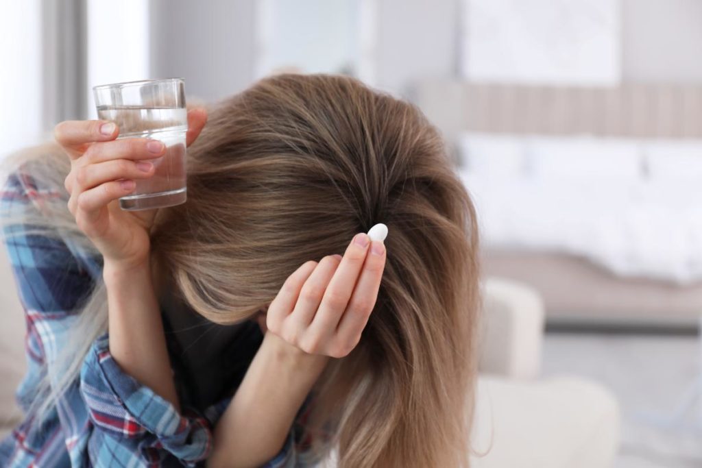 young woman distressed with a glass of water and pill in hand asking herself are you self-medicating?