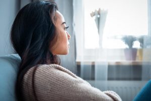 a woman sits on a couch looking out a window while thinking about the stages of opiate withdrawal