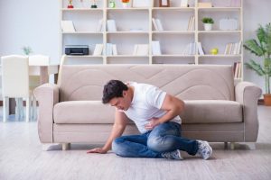 a man sits on the floor holding his stomach as he considers alcohol poisoning symptoms vs. being drunk