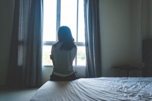 a woman sits on a bed looking out a window while wondering the signs of xanax overdose