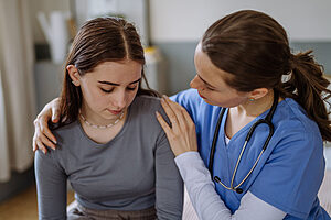 Young nurse taking care of teenage girl consoling her